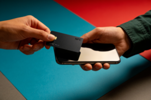 Two business professionals exchanging contact details by tapping a smart NFC business card to a smartphone at a networking event